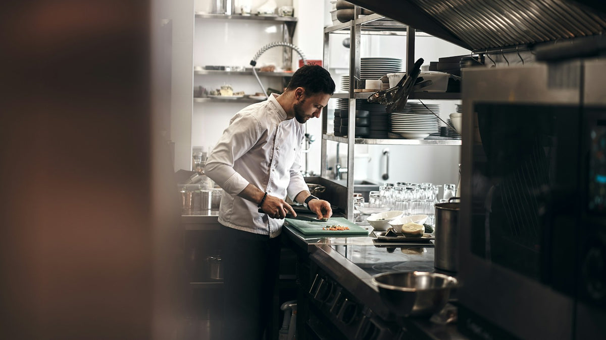 A cook chopping vegetables on a board in a kitchen
